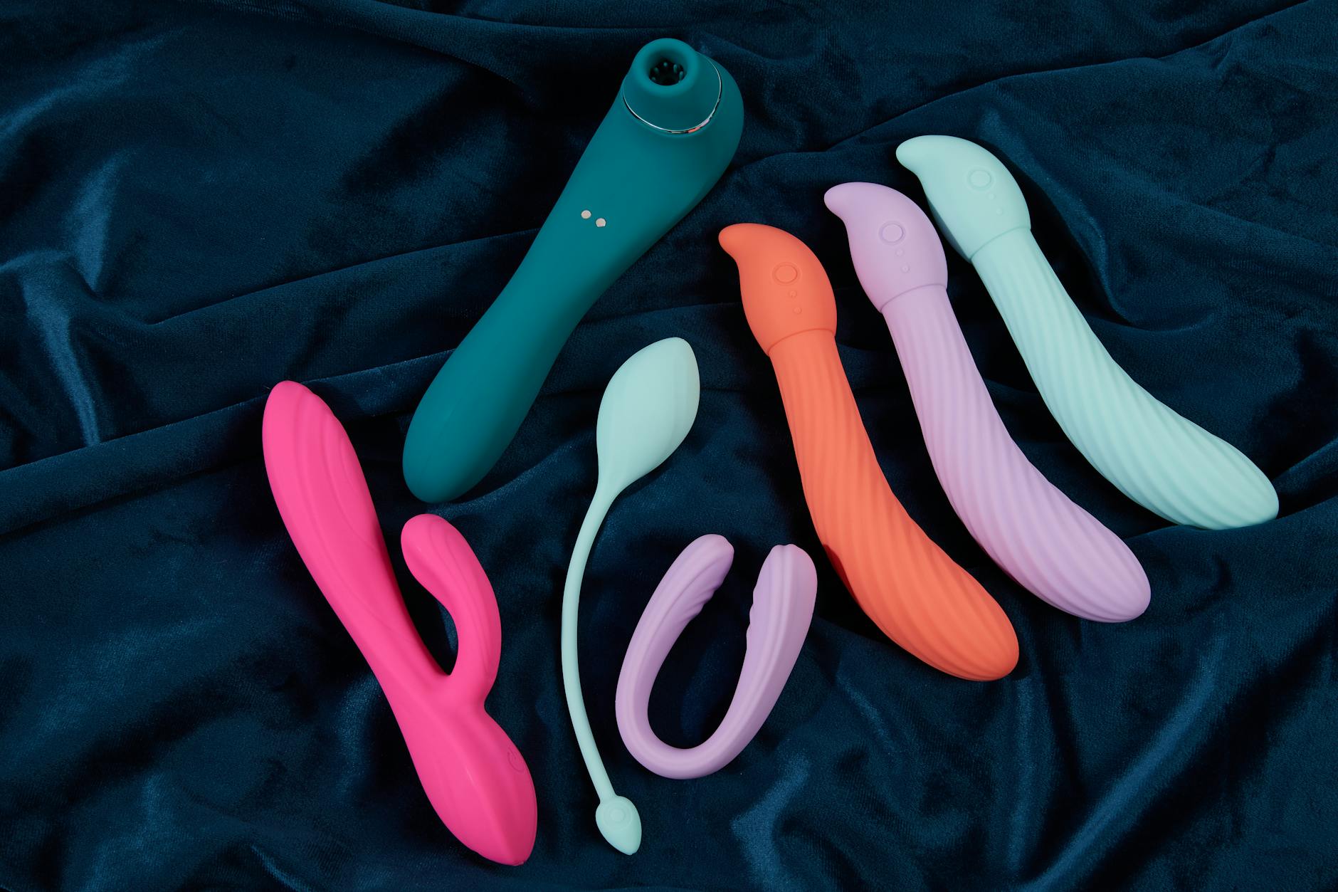 Vibradores coloridos de silicone em exibição sobre tecido azul escuro, mostrando diferentes formas e texturas
