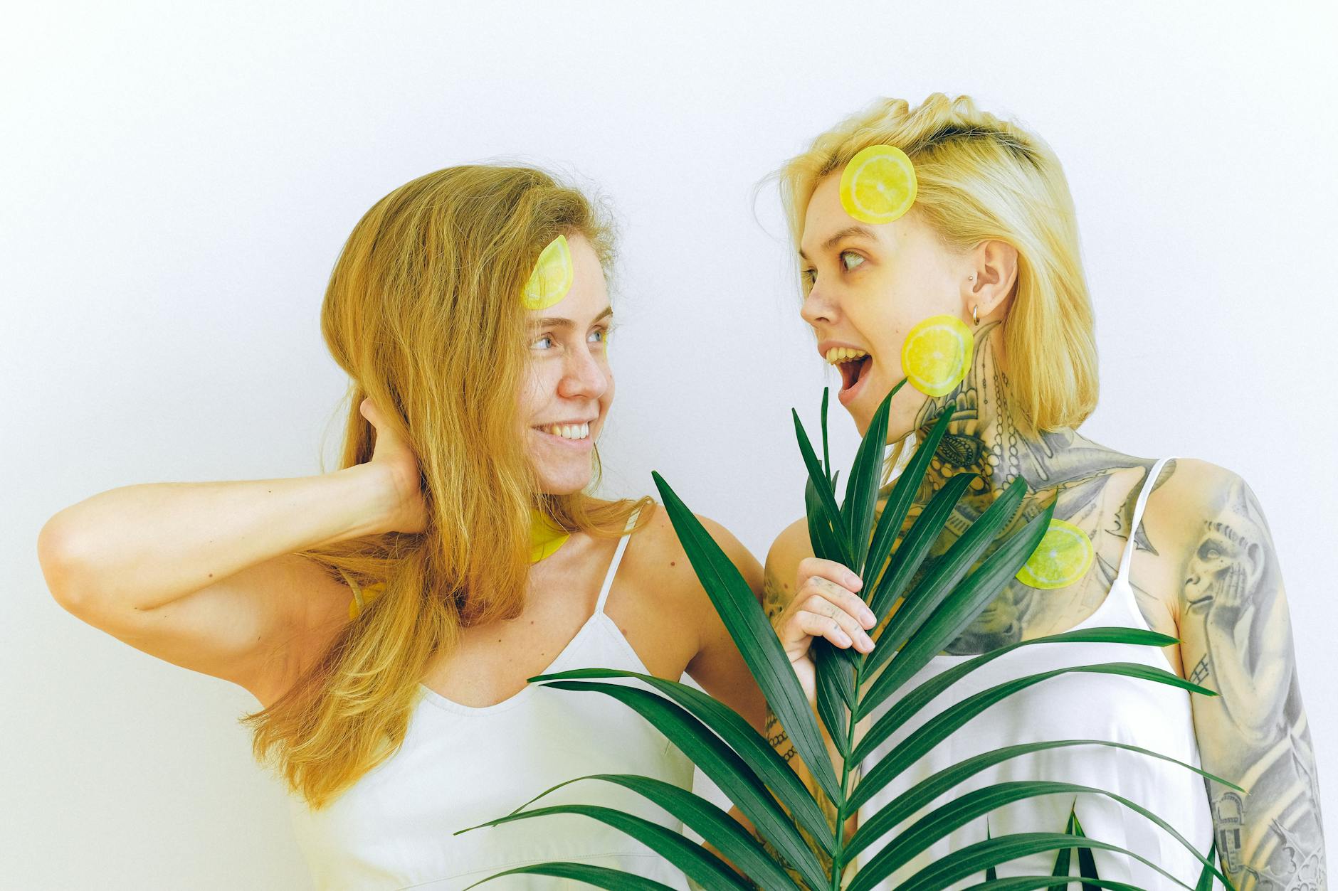 Duas mulheres sorrindo com fatias de limão e plantas tropicais, expressando alegria e diversão