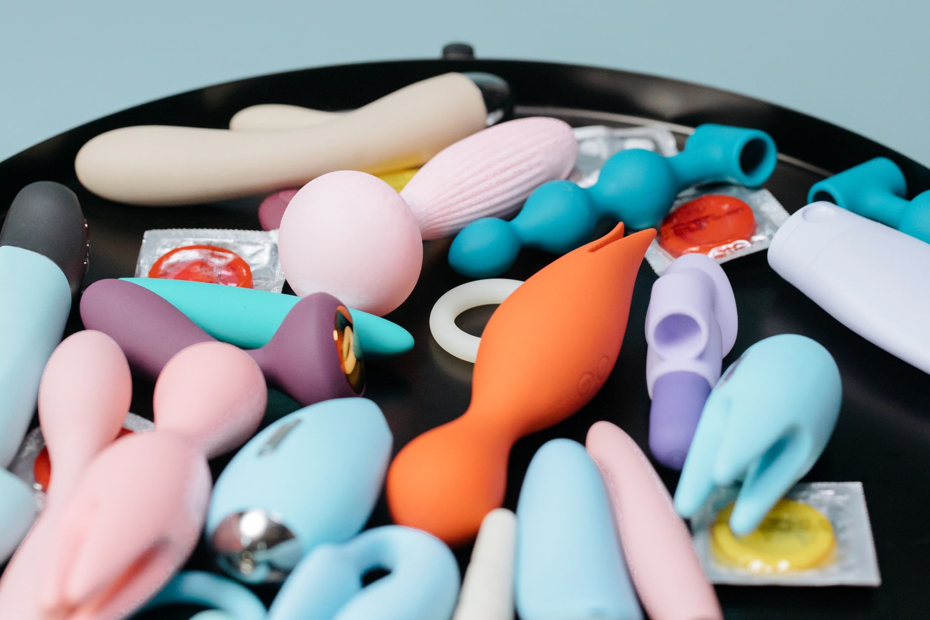 Coleção vibrante de diversos brinquedos sexuais em uma bandeja preta, apresentando formas e cores variadas.