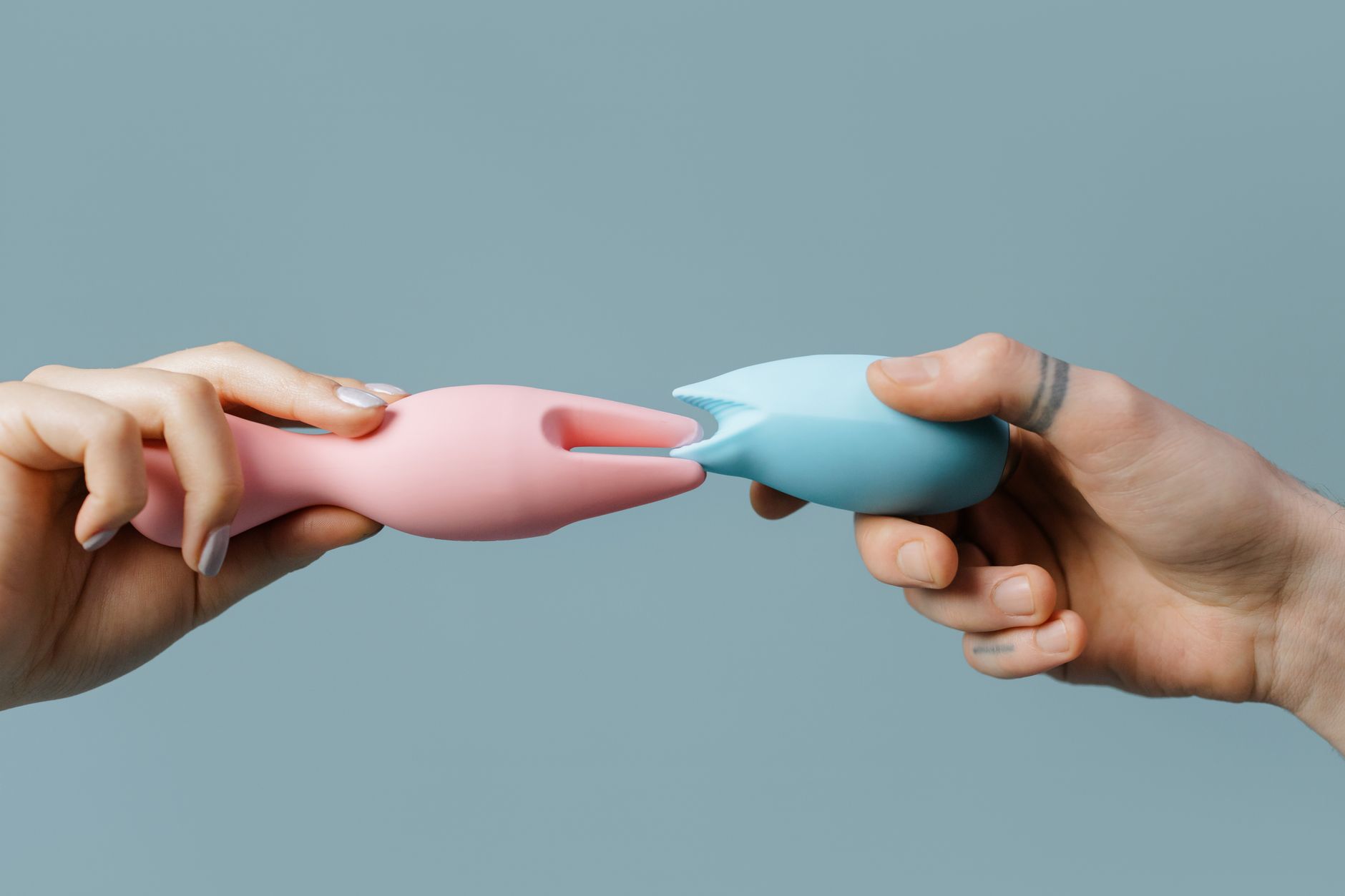 Mãos segurando vibradores de silicone em cores pastel, representando exploração segura do prazer
