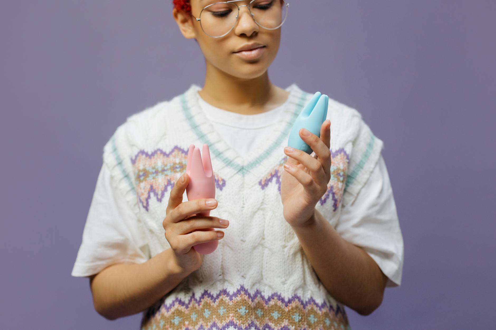 Mulher segurando vibrador de silicone azul e rosa em posição contemplativa, representando autossuficiência e autodescoberta.