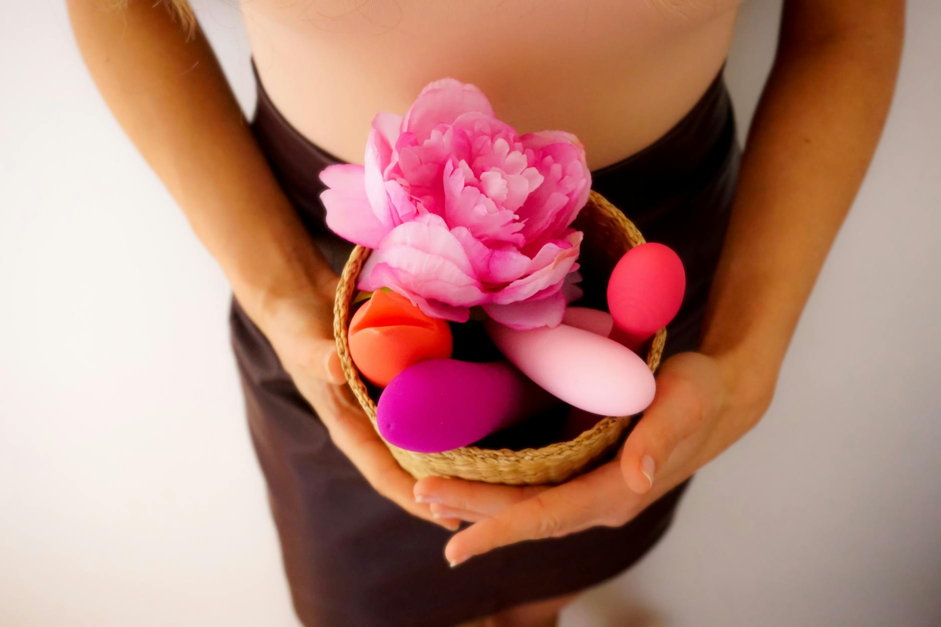 Cesta com vibradores coloridos e uma flor rosa em fundo branco